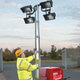 A man setting up a mini led lighting tower for use on a site.